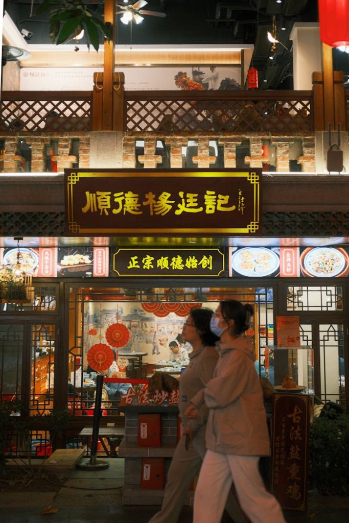 pexels photo 30842758 Traditional Chinese restaurant exterior lit at night with vibrant signage and two pedestrians walking by.