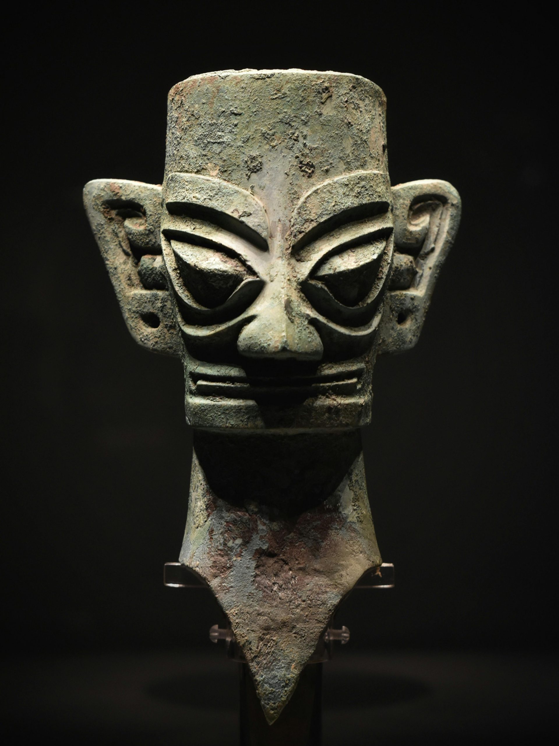 Ancient bronze Sanxingdui mask sculpture on a black background, exhibiting intricate craftsmanship.